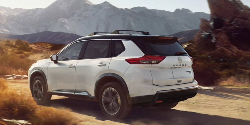 White Nissan Rogue driving off-road on a dusty desert trail.